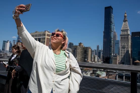 An OHIO student takes a selfie photo with a phone with the New York skyline in the background