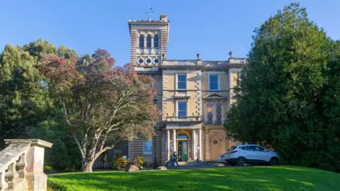 Getty Images Reed Hall, historic listed Italianate mansion, Streatham Campus, University of Exeter, Exeter, Devon, England, UK built 1867. It has a two white cars outside and a long green lawn.