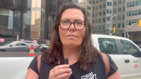 A woman holds a microphone and speaks to a reporter