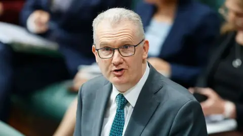 Getty A middle aged man with white hair and glasses, wearing a suit, talks in parliament