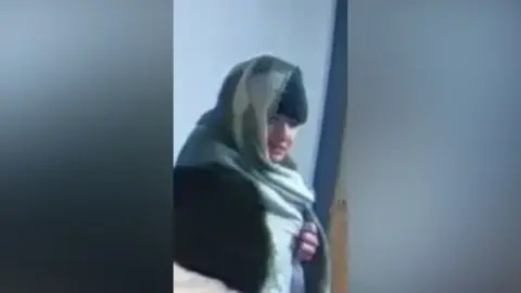 Lancashire Police A grainy still from CCTV showing Owens in a corridor in Carla's flat block. He has a green blanket over his head and is wearing a black beanie hat, but his face is exposed and pointing towards the camera.